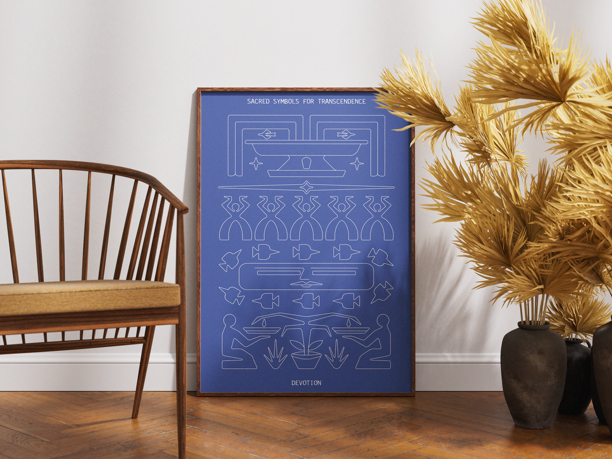 A framed art print featuring white line-art tribal symbols and diagrams on a blue background, leaning against a white wall on a wooden floor next to a wooden chair and pampas grass in a vase.
