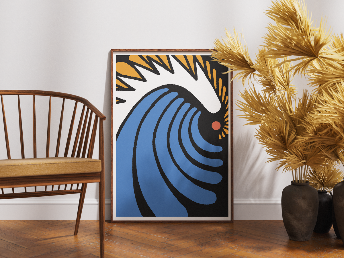 A framed abstract art print featuring a stylized blue wave and sunburst design, leaning against a white wall on a wooden floor next to a wooden chair and potted palm trees.
